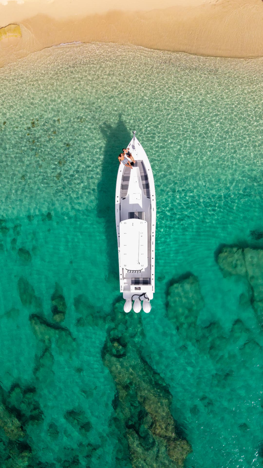 Overhead drone shot of guests on the bow while anchored over turquoise sand