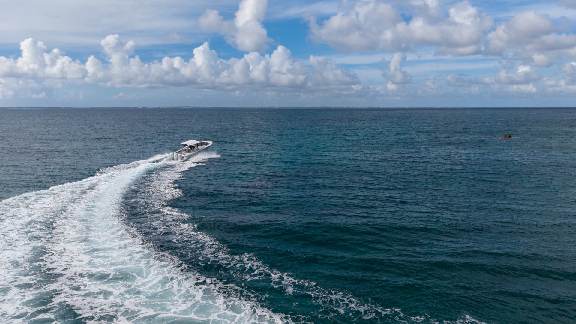 Wide drone shot of the boat carving a wake across open water