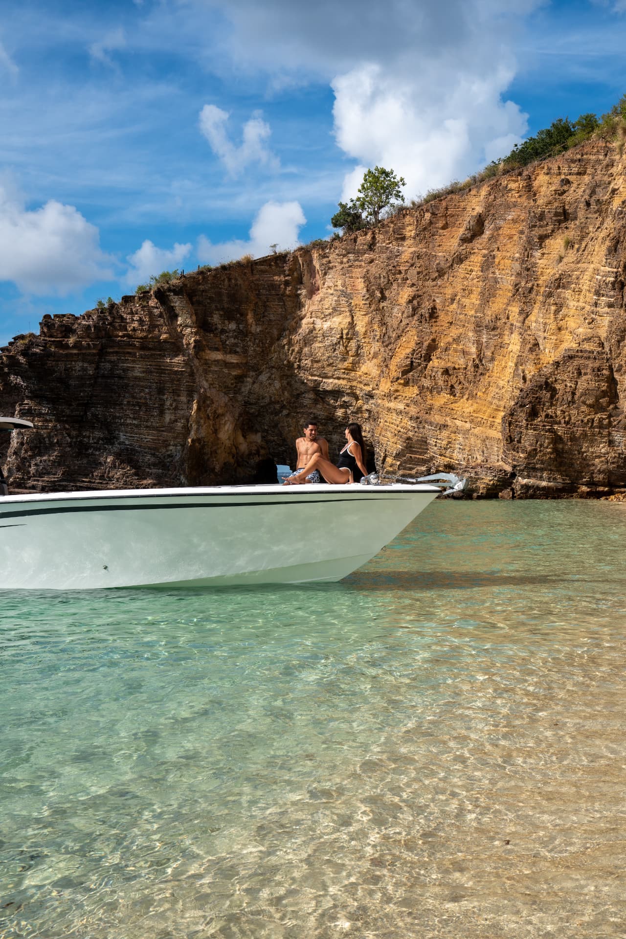 Guests on the bow in a secluded cove beneath golden cliffs